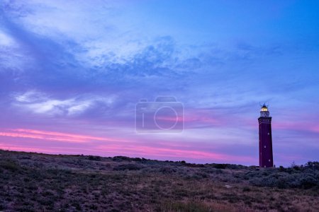 Dieses eindrucksvolle Bild zeigt die Silhouette eines Leuchtturms vor einem dramatischen Himmel bei Sonnenuntergang, der in leuchtenden Violett- und Rosatönen gemalt ist. Leuchttürme leuchten hell, ein Symbol der Orientierung