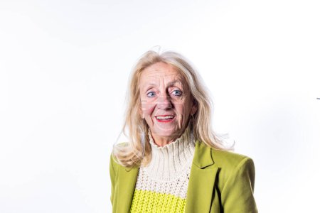 Cette image présente une dame blanche âgée avec un sourire chaleureux et de longs cheveux blonds. Ses yeux bleus véhiculent un sentiment de convivialité et d'ouverture. Elle est vêtue à la mode d'un pull en tricot blanc et