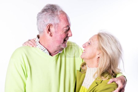 Das Bild fängt einen intimen Moment zwischen einem älteren kaukasischen Paar ein, das sich liebevoll in die Augen blickt. Der Mann mit den grauen Haaren trägt einen hellgrünen V-Ausschnitt-Pullover über einem