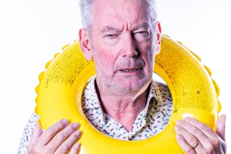 En esta imagen lúdica, un hombre mayor con una expresión escéptica está enmarcado por un anillo de natación de color amarillo brillante. El contraste entre su expresión y el símbolo típico del ocio y la relajación proporciona una