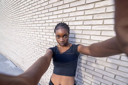 This image captures a young African woman taking a dynamic wide-angle selfie. The perspective is emphasized by her extended arm holding the camera, leading to a slight distortion that adds to the