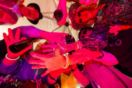 This vivid image captures a moment of celebration, viewed from above, as a group of friends come together in a dynamic toast. Their hands, clinking bottles and glasses, are the focal point, set