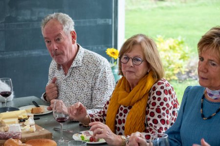 This image shows a group of seniors enjoying a cheese tasting. The man in the forefront, with an expressive face, seems to be savoring the flavor or perhaps giving his approval of the selection. The