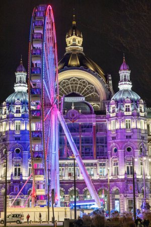 Photo for Antwerp, Belgium, January 25th, 2024, A dazzling Ferris wheel lights up the night, towering in front of the Antwerp Central Station. The ornate facade of the station, with its domes and stonework, is - Royalty Free Image