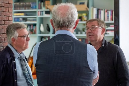 This image offers a glimpse into a moment of engrossed conversation among three senior male friends. We see the men from over the shoulder of one, focusing on the two others who are attentively