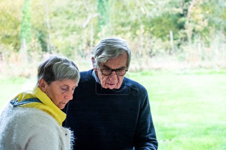 This photograph captures an intimate moment of an elderly couple walking side by side, immersed in a conversation or shared silence. The man, wearing glasses and a dark sweater, appears to be
