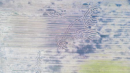 This aerial image displays the textured patterns of snow-covered crop fields, interrupted by the elegant curves of tractor tracks. The tracks create an abstract design, reminiscent of brush strokes on