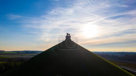 Photo for Waterloo, Brussels, Belgium, February 25th, 2024, The photograph captures the iconic Lions Mound at Waterloo, silhouetted against a brilliant sunburst. The sun, positioned directly behind the statue - Royalty Free Image