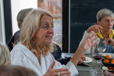 Dieses Bild zeigt eine ältere Dame in einer weißen Bluse, deren Gesicht vom Nervenkitzel beseelt ist, eine fesselnde Geschichte zu erzählen. Ihre Hände gestikulieren ausdrucksstark und unterstreichen die Energie der Erzählungen. Ein Gleichaltriger