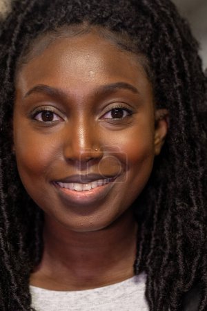 La photographie capture une jeune femme noire avec un sourire doux et confiant. Sa coiffure naturelle twist-out encadre parfaitement son visage lumineux, soulignant ses yeux qui scintillent de vivacité. L '