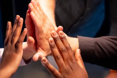 L'image représente un groupe de mains réunies en un groupe de cinq, symbolisant le succès de l'équipe, l'unité et la collaboration. La diversité au sein de l'équipe est évidente à travers la variété des tons de peau