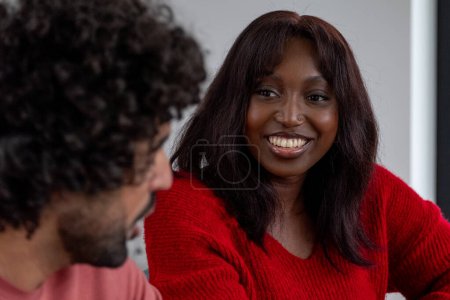 Dieses Foto fängt eine afroamerikanische Frau mit einem strahlenden Lächeln ein, die anscheinend in ein angenehmes Gespräch verwickelt ist. Ihr warmes, echtes Lächeln und ihr direkter Blickkontakt deuten darauf hin, dass sie tief verbunden ist.