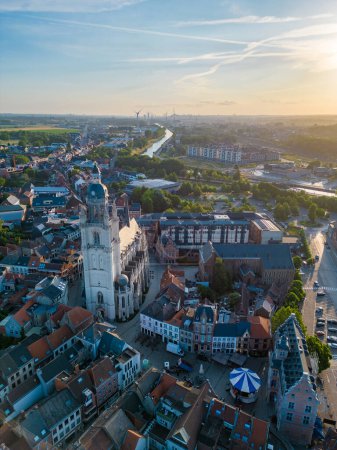 Le soleil couchant jette une douce lueur sur la ville de Halle, en Belgique, dans cet instantané aérien qui capture l'essence des villes d'une beauté durable. Au centre de l'image se trouve le magnifique
