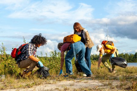 This inspiring image captures a group of environmentally conscious friends, from diverse ethnic backgrounds including Caucasian and Black, participating in a lakeside cleanup. Each person is actively