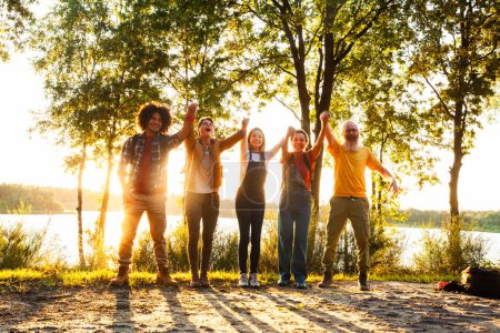 Sobre el radiante telón de fondo de un sol poniente, esta imagen resume la celebración de un grupo de amigos junto al lago. Con los brazos levantados triunfante y sonrisas brillantes a través de su