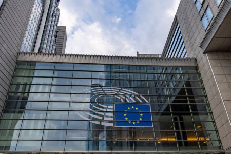 Foto de BRUSELAS, BÉLGICA, 23 de junio de 2023: Una vista de un edificio contemporáneo que exhibe la bandera de la Unión Europea, en un contexto de cielo parcialmente nublado. Bandera de la Unión Europea en la fachada del edificio moderno - Imagen libre de derechos