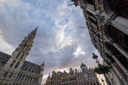 Foto de Bruselas, Bélgica, 23 de junio de 2023, Capturando la esencia de la Grand Place de Bruselas, esta imagen destaca la imponente torre gótica y los edificios barrocos adornados bajo un cielo expresivo al atardecer. Majestuoso - Imagen libre de derechos
