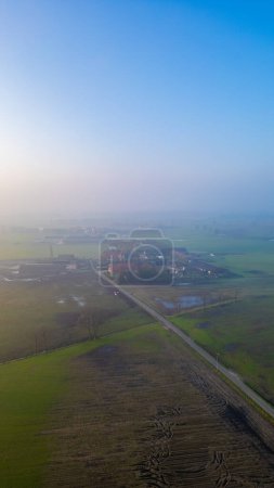 A vertical slice of dawns tranquility captures a sleepy hamlet awakening amid the soft caress of morning fog, as seen from above. Misty Morning Ascend Over Sleepy Countryside Hamlet. High quality