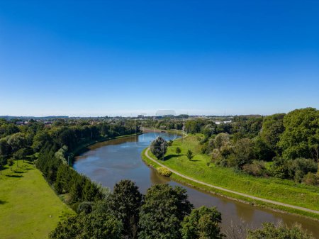 Téléchargez les photos : Cette image offre une vue aérienne splendide d'une rivière sinueuse traversant un paysage verdoyant sous le ciel bleu clair. Les rives sont bordées d'arbres verdoyants et d'herbe, accentuant la - en image libre de droit