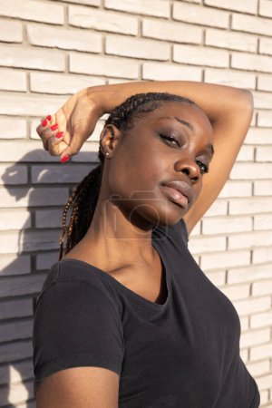 The image showcases an African woman in a casual black t-shirt, with her arm raised and hand gently resting on her head, giving off a relaxed and serene vibe. The sunlight softly highlights her