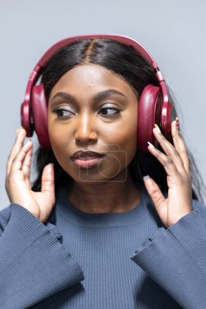The image showcases a young African American woman immersed in music, wearing red over-ear headphones. Her eyes are gently closed, signaling she is savoring the sound, which could be a favorite song