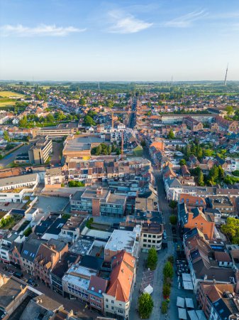 This is an aerial image capturing the heart of Halle, Belgium, in the gentle embrace of the golden hour. The towns historic charm interweaves with modern updates, as terracotta rooftops mingle with