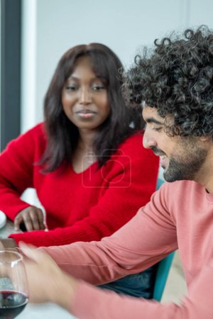 This image captures a slice of life from an indoor social gathering. The focus is on a man, possibly of Middle Eastern or Hispanic ethnicity, with distinctive curly hair and a salmon-colored shirt