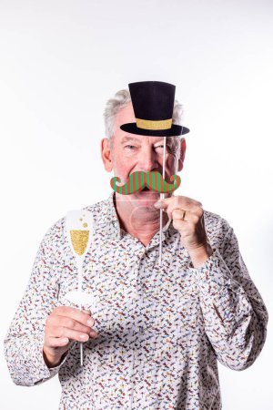 Ein älterer Mann hält spielerische Partyrequisiten, Zylinderhut und gestreiften Schnurrbart hoch, während er ein Champagnerglas in der Hand hält, was auf eine feierliche Stimmung vor einem weißen Hintergrund hindeutet.
