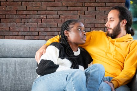 In this image, we see an African American woman and a Middle Eastern or Hispanic man sharing an intimate moment. The woman, dressed in a cozy black and white sweater, is seated and looking at her