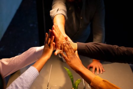 L'image montre un groupe de mains de personnes de différentes ethnies s'engageant dans un collectif cinq au-dessus d'une table de réunion, mettant en évidence un moment de succès de l'équipe ou d'accord au sein d'un