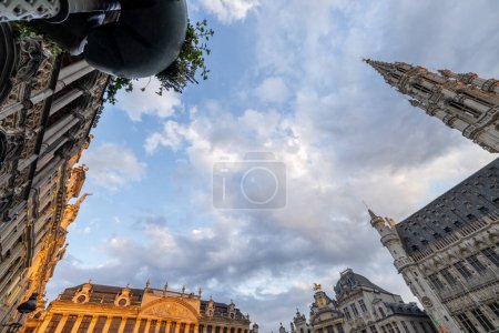 Brussels, Belgium, June 23, 2023, This low-angle shot offers a sweeping view of the ornate facades and soaring towers of Grand Place in Brussels, framed by a dynamic sky with soft evening light