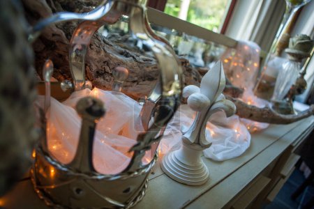 Ein silberner Vintage-Spiegel spiegelt eine schön arrangierte Interieur-Szene wider, komplett mit warmen Feenlichtern, die über rustikalem Holzdekor drapiert sind. Ein weißes skulpturales Element verleiht dem gemütlichen Ambiente eine künstlerische Note
