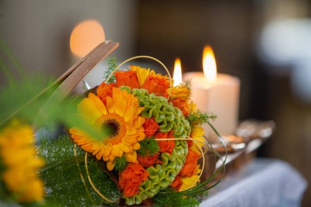 This image focuses on a floral centerpiece, featuring bright orange flowers and intricate greenery, complemented by the ambient glow of nearby candles. The soft lighting enhances the natural colors