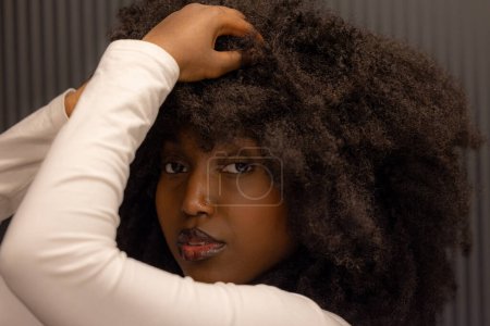 Une image en gros plan mettant en vedette une femme afro-américaine avec une magnifique coiffure afro. Elle pose la main levée sur la tête, apportant confiance et assurance. Le réglage intérieur avec neutre