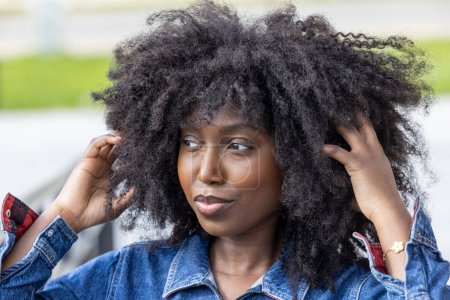 A close-up captures a stylish African American woman in a denim outfit, her natural hair framing her face. Her sidelong glance and the subtle play of light on her features create a compelling portrait