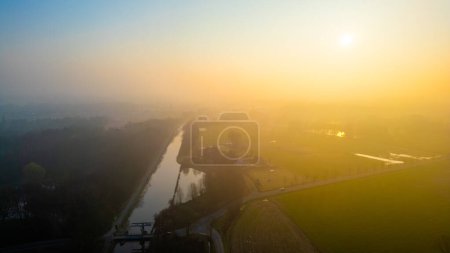 The break of day casts a golden hue over a meandering canal, with the gentle mist enhancing the tranquil rural ambiance. Sunrise over Canal with Soft Mist in the Countryside. High quality photo