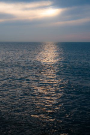 This image encapsulates the ethereal beauty of the ocean under a sky with sunlight struggling to break through the cloud cover. The subdued sun casts a diffuse, mystical light on the water, creating a