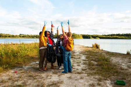 Un animado grupo de voluntarios celebra su contribución a la naturaleza mediante la limpieza de una orilla de los lagos. El equipo voluntario levanta las manos con júbilo después de la limpieza de la costa. Foto de alta calidad