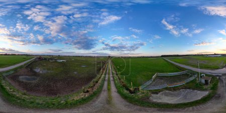 Téléchargez les photos : Un panorama à 360 degrés révélant une route de ferme sans fin sous un vaste ciel nuageux, incarnant l'essence des espaces ouverts. Campagne panoramique : Ciel étendu sur une route agricole étroite. Haute qualité - en image libre de droit