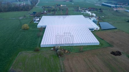 Foto de Duffel, Bélgica, 20 de marzo de 2024, Capturada desde el cielo al atardecer, esta imagen muestra la expansión de un gran complejo de invernadero en medio de las tierras de cultivo pastorales. El gran tamaño del complejo - Imagen libre de derechos