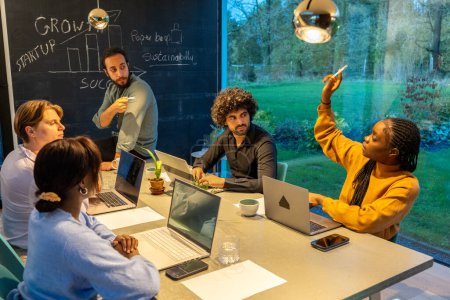 Un grupo de emprendedores multiétnicos se involucra en una inspiradora sesión de lluvia de ideas en un espacio de oficina moderno y bien iluminado. Discuten el crecimiento, el éxito de las startups y la sostenibilidad, como lo indica el