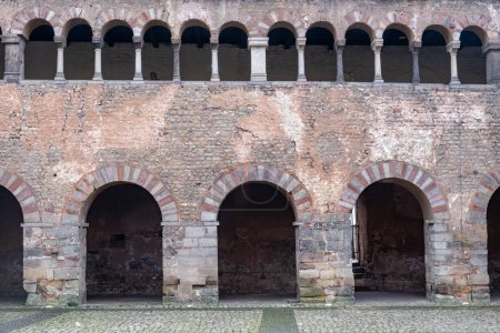 Esta imagen captura el encanto histórico de una estructura de piedra medieval o romana con arcos repetitivos y una fila de ventanas arqueadas arriba. Los patrones de piedra y ladrillo bien conservados evocan un sentido