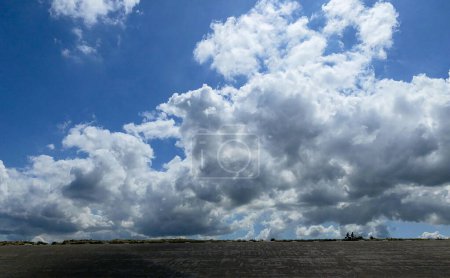 The image presents a striking view of expansive cumulus clouds filling the sky above a low horizon. The stark contrast between the billowing white clouds and the clear blue sky emphasizes the vastness
