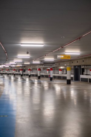 This image portrays the quiet vastness of an empty underground parking lot. The polished concrete floor reflects the evenly spaced fluorescent lights above, creating a pattern of light and shadow. The