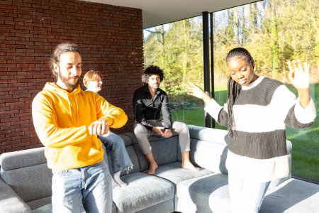 In a living room bathed in sunlight, a diverse group of friends is engaged in a lively conversation. One man checks the time, perhaps indicating its time for an event, while a woman gestures