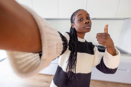 This is an engaging selfie of a confident woman in a stylish striped sweater giving a thumbs-up to the camera. The wide-angle perspective creates a dynamic feel, placing the viewer in her intimate