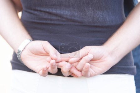 Esta imagen se centra en las manos de un hombre unidas frente a él, transmitiendo una postura relajada e informal. Los detalles de sus manos se destacan contra la sencillez de su camisa oscura y