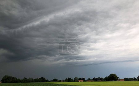 La imagen captura vívidamente el dramático contraste entre las oscuras nubes de tormenta y el tranquilo entorno rural de abajo. Las nubes inminentes sugieren una tormenta inminente, añadiendo una dinámica y