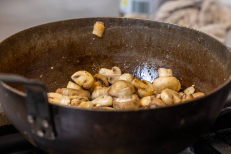 En esta imagen, los champiñones descuartizados están siendo salteados en una sartén de hierro fundido sazonada, con un enfoque en las verduras brillantes que indican que se cocinan a la perfección. El fondo es suave