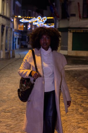 Este retrato captura a una mujer mientras da un paseo nocturno por un callejón de la ciudad, adornado con luces festivas centelleantes. La suave iluminación del entorno resalta suavemente su figura y